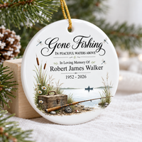 Personalized memorial ornament leaning against a small wooden block surrounded by pine and warm lights