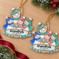 Two personalized acrylic Christmas tree ornaments with snowman designs laid out on a light wood surface alongside holiday