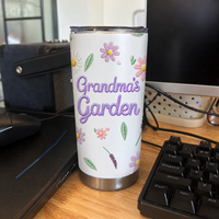 A single white custom name tumbler standing on a wooden desk near a computer keyboard.
