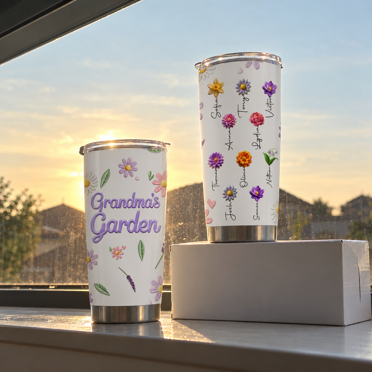 Two personalized stainless steel tumblers on a windowsill against a sunset sky.