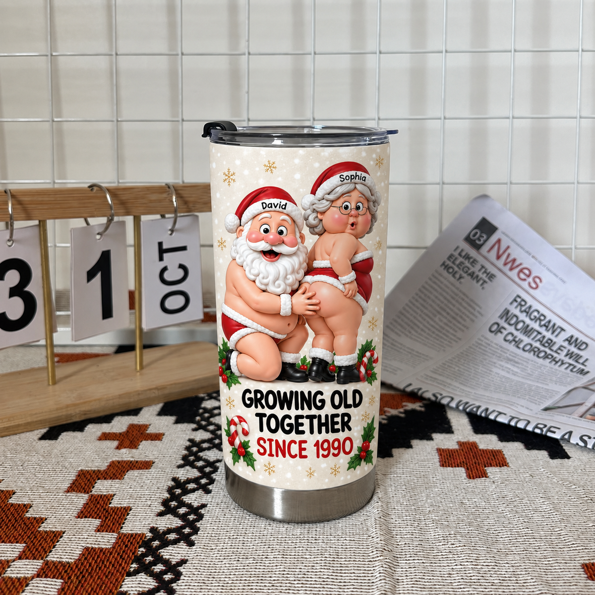 Funny Santa tumbler standing on woven fabric next to desk calendar and newspaper in indoor setting.