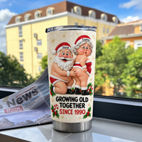 Personalized anniversary gift tumbler displaying naughty Santa graphic beside a newspaper and buildings.