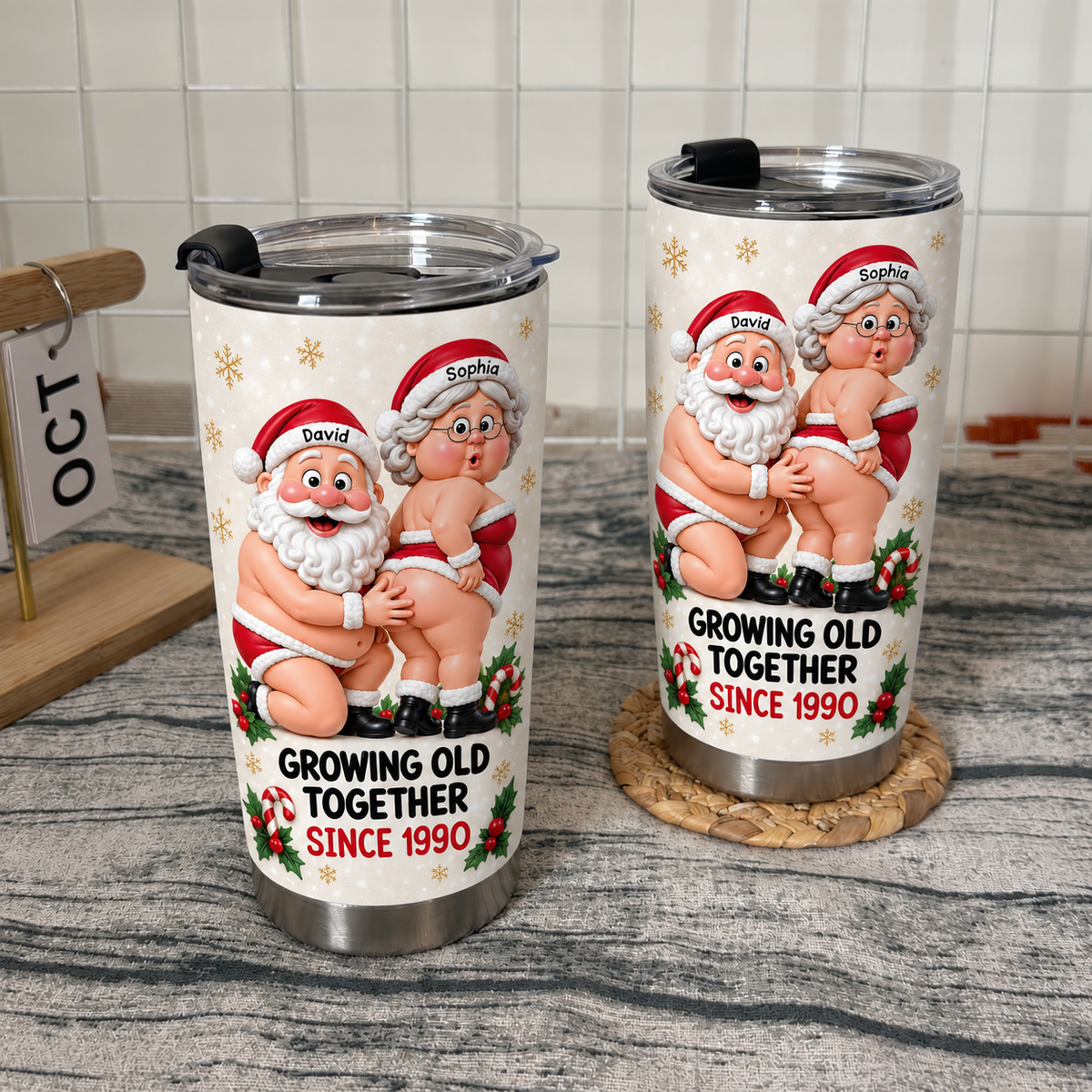 Two stainless steel tumblers with humorous Santa and Mrs. Claus design showcased on wooden shelving.