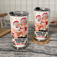 Two stainless steel tumblers with humorous Santa and Mrs. Claus design showcased on wooden shelving.
