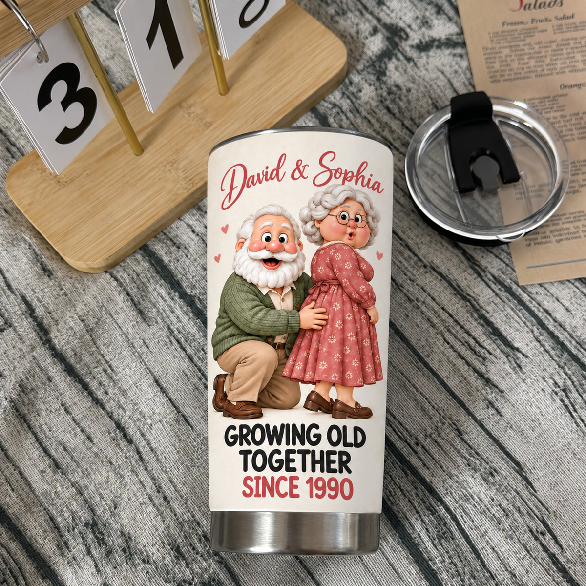 White stainless steel travel tumbler with cartoon elderly couple graphic and David & Sophia text next to its black lid and a