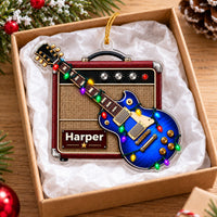 A personalized blue guitar amp acrylic Christmas ornament resting inside a gift box filled with white tissue paper.