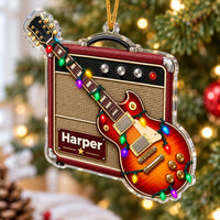 A personalized red guitar amp acrylic Christmas ornament hanging from a festive green pine branch.