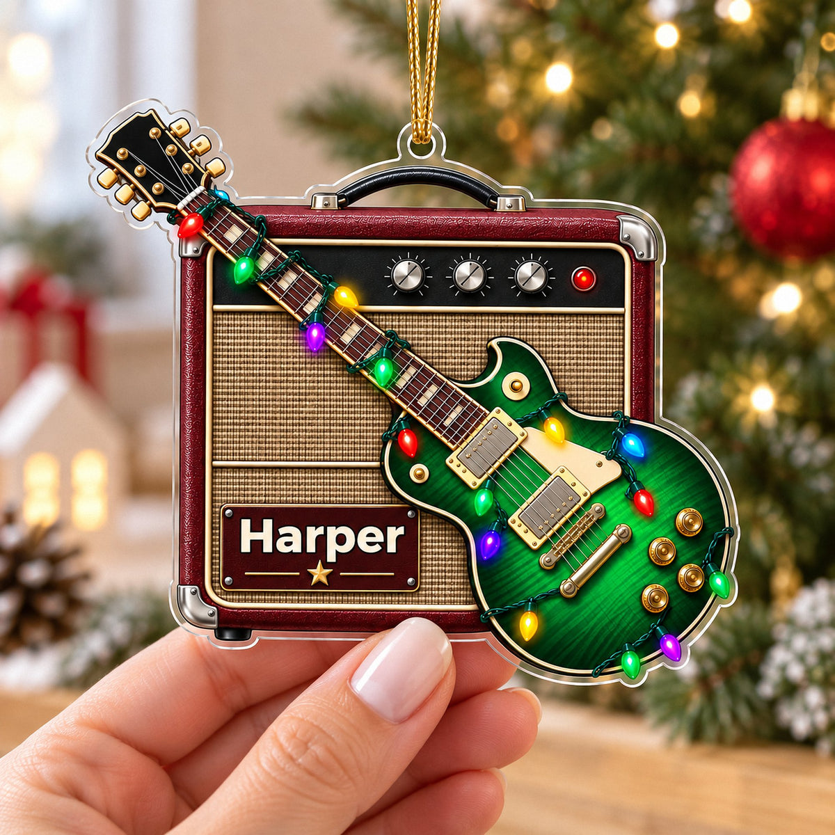 A person holding a personalized green guitar amp acrylic Christmas ornament in front of a decorated tree.