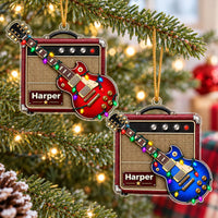 Two personalized guitar amp acrylic Christmas ornaments hanging on a pine tree with warm lights, featuring red and blue