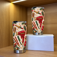 Two personalized hair stylist tumblers with red styling tools and pine details stand on a wooden shelf inside a lit cabinet.