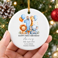 Hand holding the personalized baby gift ornament with a watercolor safari jungle design against a pine tree background.