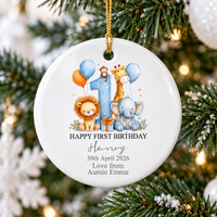 Happy First Birthday ornament featuring watercolor safari animals hanging on a festive Christmas tree with glowing lights.