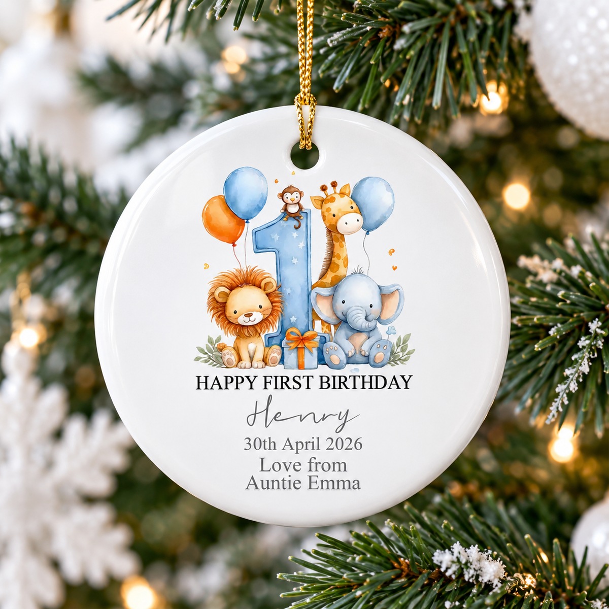 Happy First Birthday ornament featuring watercolor safari animals hanging on a festive Christmas tree with glowing lights.