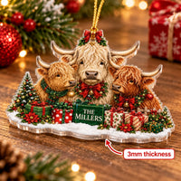 Close-up of the Highland Cow Family Christmas Ornament resting on a rustic wooden table near pine needles.