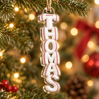Vertical name ornament with baseball stitch lettering hanging on a glowing Christmas tree.