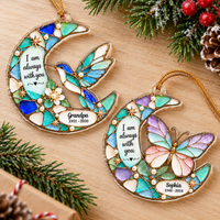 Two custom memorial ornaments with hummingbird and butterfly designs displayed on a rustic wooden tabletop next to pine