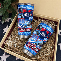Two personalized hockey gear tumblers nestled in a gift box filled with paper shred filler and a pine tree branch.