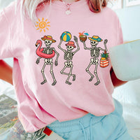 Model wearing a pastel pink t-shirt printed with dancing skeletons at the beach.