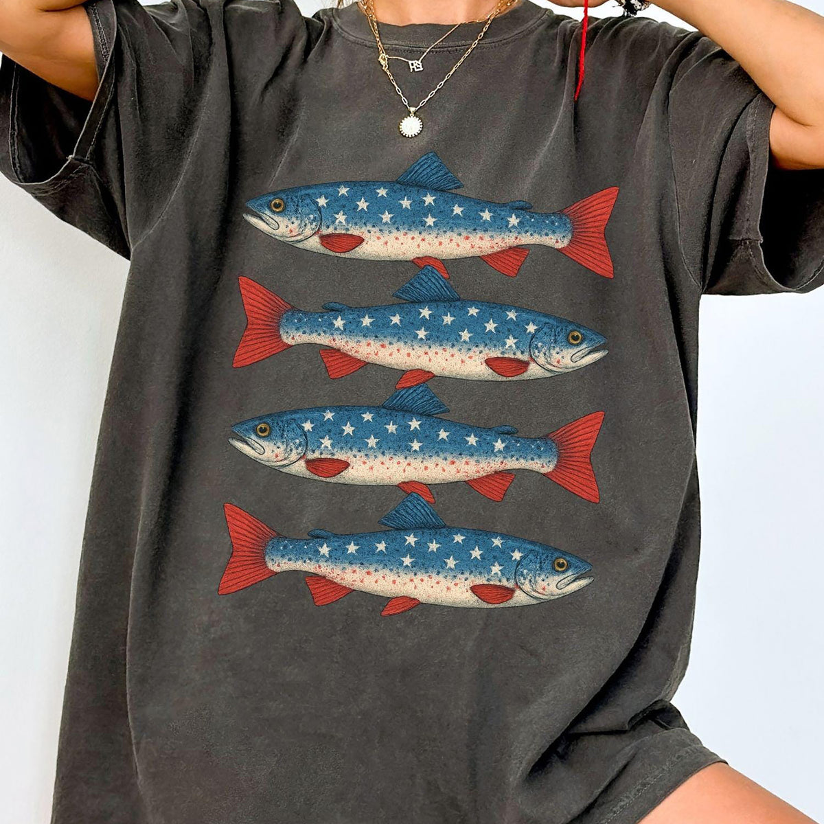A woman wears a faded charcoal t-shirt featuring a vintage graphic of four trout fish patterned with American flag stars and