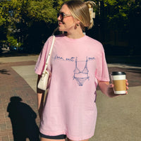 A woman wearing a pink graphic t-shirt with a blue bikini and clothesline design, holding a coffee cup outdoors.