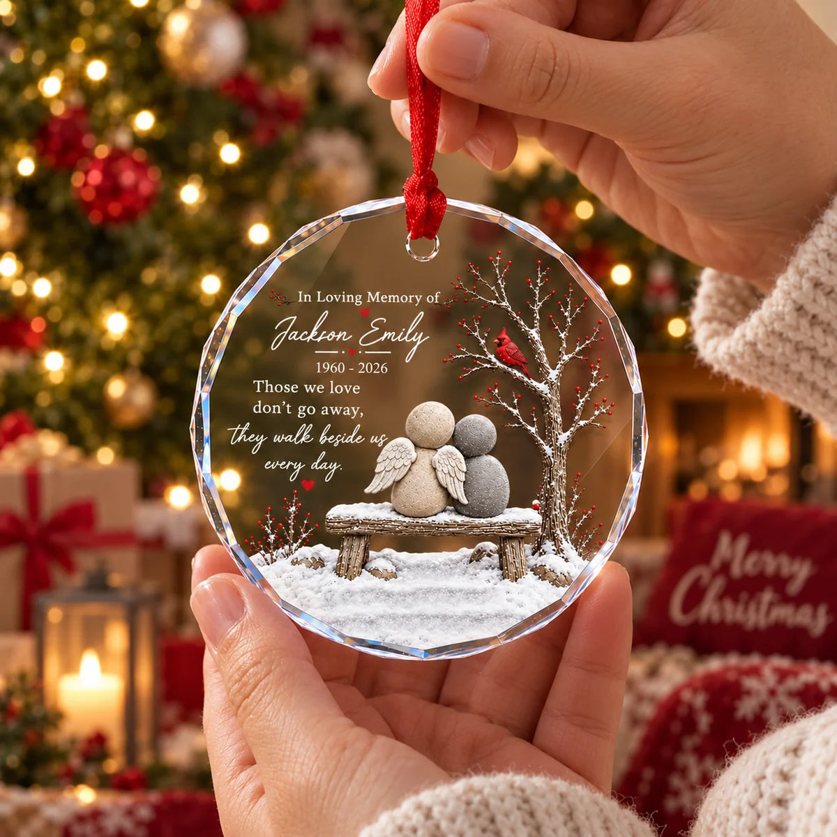 Hands holding a round clear glass memorial ornament in front of a glowing Christmas tree.