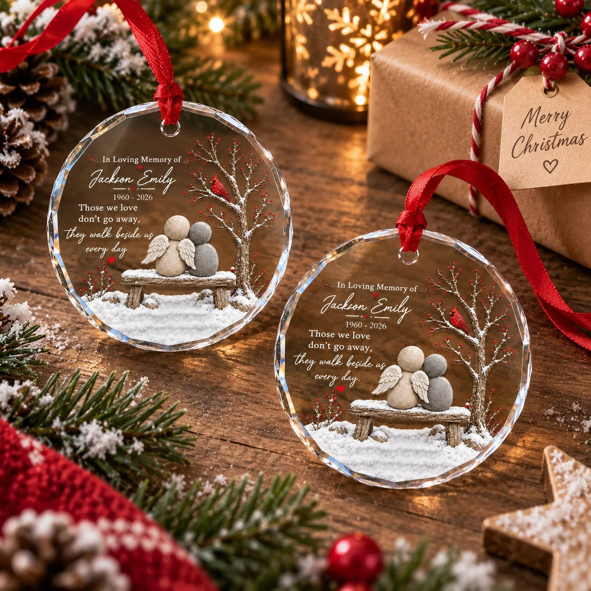 Two personalized glass ornaments resting on rustic wooden surface beside gift and pine branches.