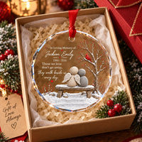 Round clear glass memorial ornament inside open gift box with red ribbon and tissue paper.