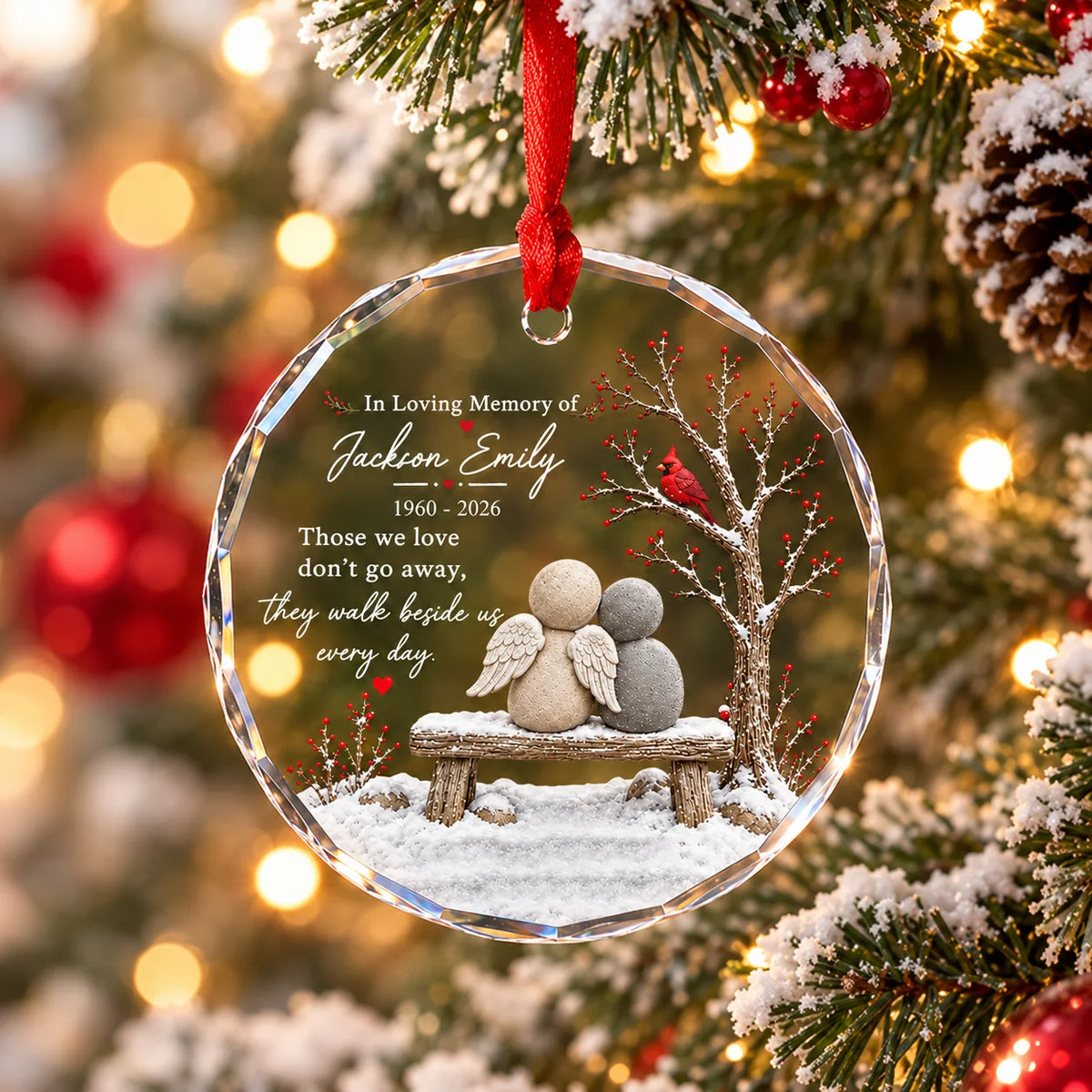 Personalized In Loving Memory glass ornament hanging on Christmas tree with warm lights and snow backdrop.