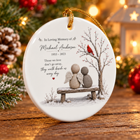 Round bereavement ornament standing upright on a wooden table near pine needles and warm bokeh lights.