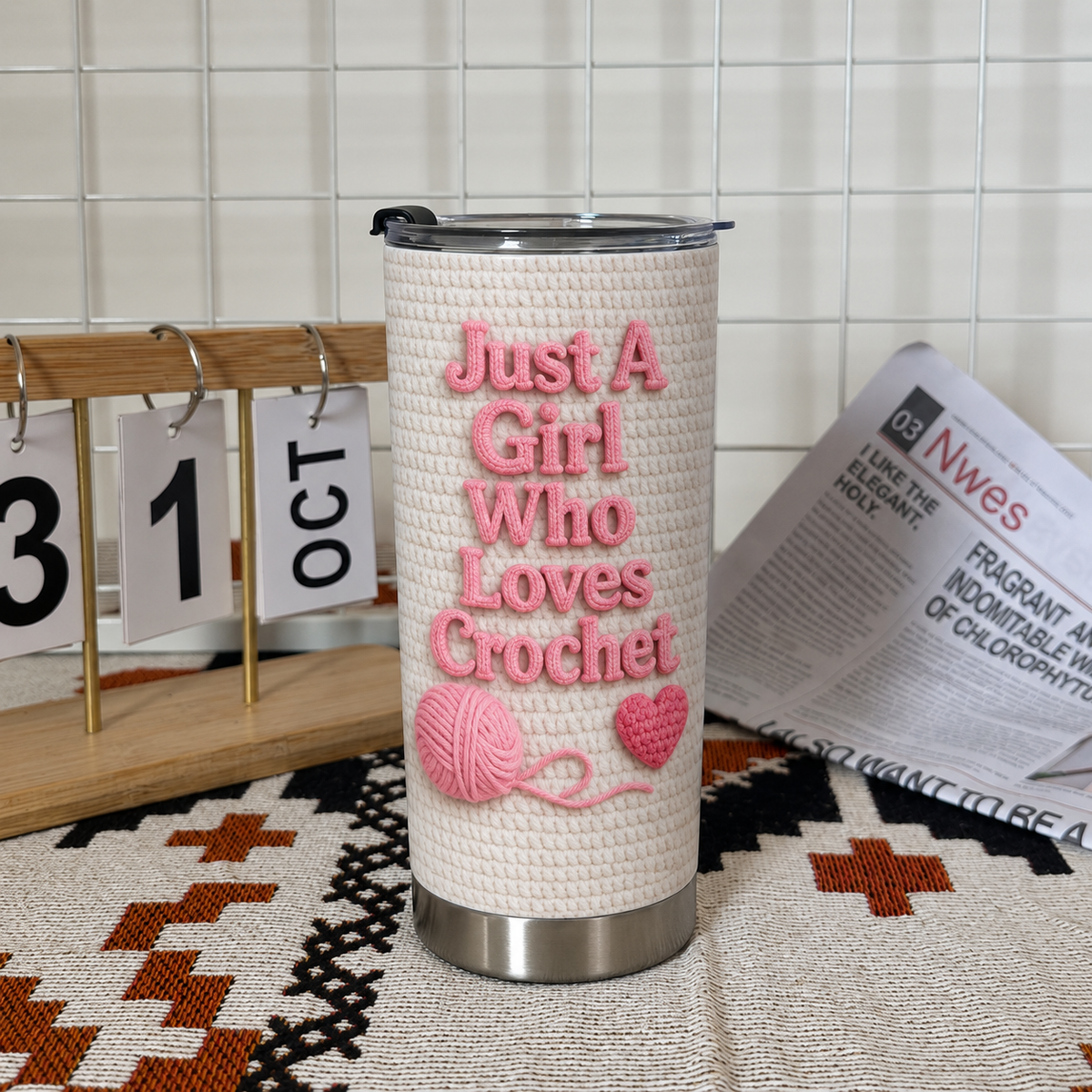 Personalized insulated stainless steel cup standing on patterned textile next to calendar block and newspaper.