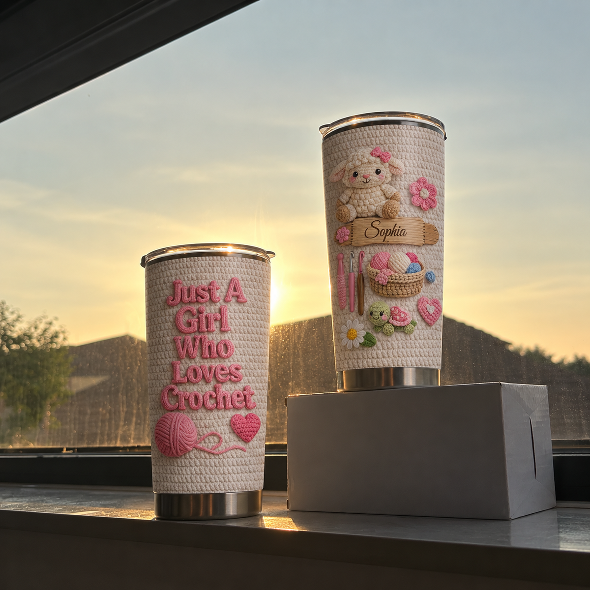 Two personalized insulated stainless steel cups on windowsill against a sunset sky, showcasing cute crochet details.