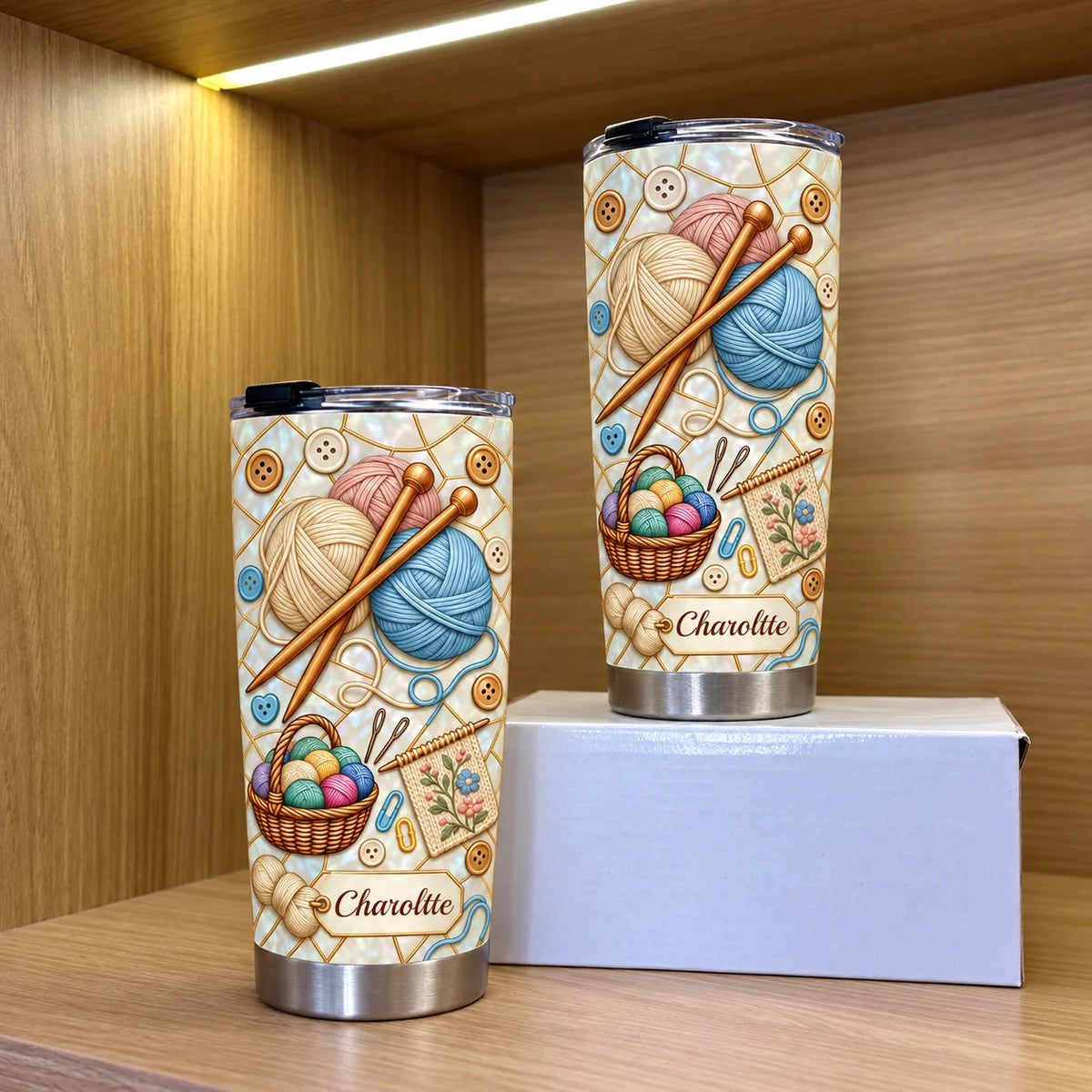 Two personalized stainless steel tumblers with knitting yarn design displayed on a white box inside a wooden shelf.