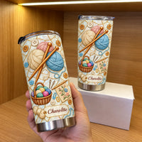 A hand holding a personalized knitting yarn stainless steel tumbler with another tumbler on a box in the background.