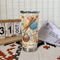 Insulated stainless steel tumbler with knitting yarn design standing upright on a textured mat next to a desk calendar and