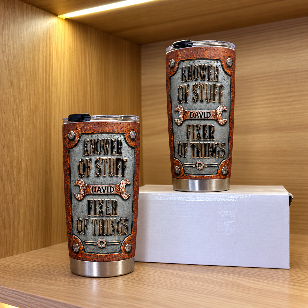 Two personalized tool themed tumblers in different sizes stand on a white box inside a wooden cabinet.