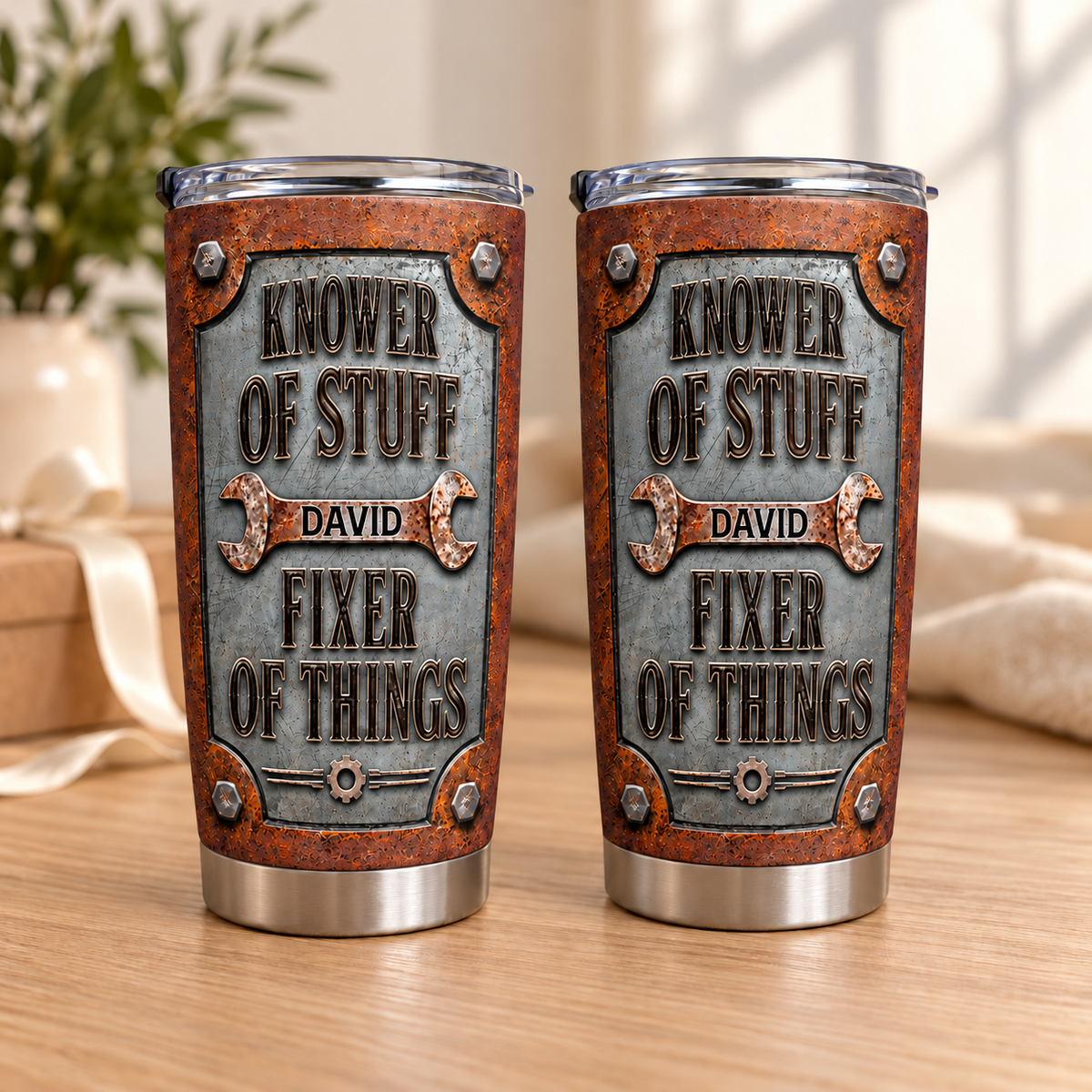 Two stainless steel tumblers with custom mechanic text stand upright on a wooden table with soft indoor lighting.