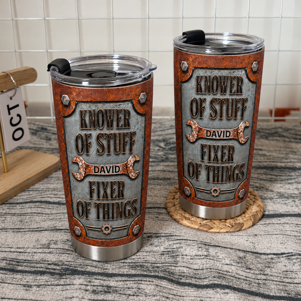 Two industrial style dad tumblers with wrench graphics sit on a wooden surface next to a wire grid wall.