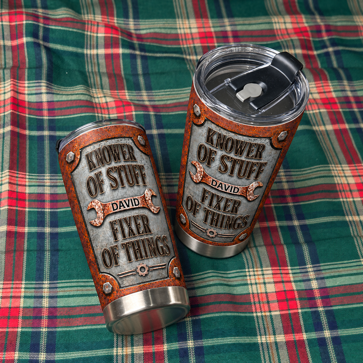 Two personalized dad tumblers rest diagonally on a green and red plaid fabric background.