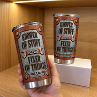 A hand holds a custom stainless steel tumbler featuring a rust and silver tool design with Knower of Stuff Fixer of Things