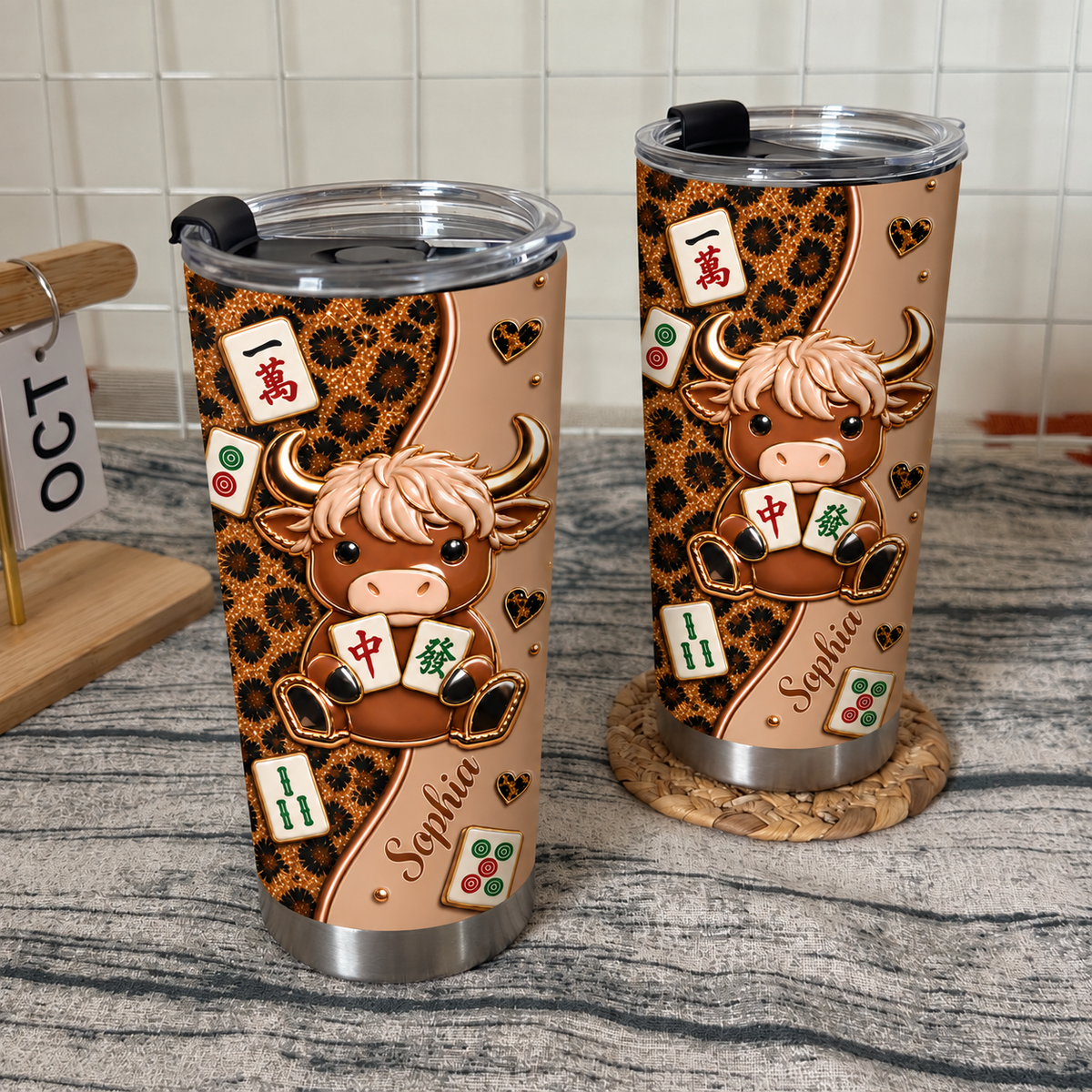 Two leopard print cow mahjong tumblers displayed on white wire grid background with wooden stand.