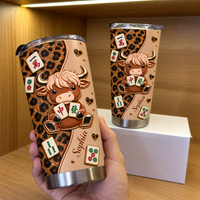 Hand holding leopard print cow mahjong tumbler on wooden shelf with second custom name tumbler on box.