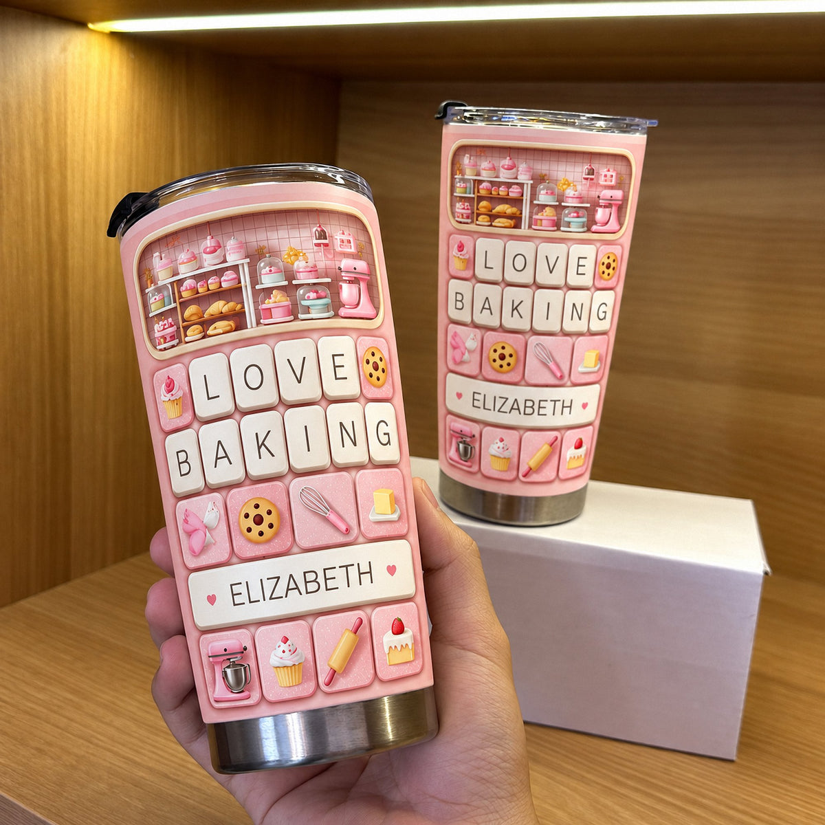 Close-up of a baking enthusiast gift tumbler held in a hand with a second tumbler on a white box behind it.