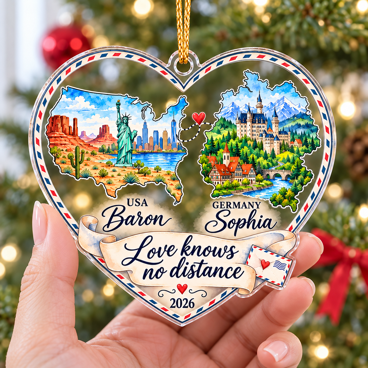 Hand holding a personalized acrylic heart ornament with USA and Germany maps connected by a dotted line and red heart.