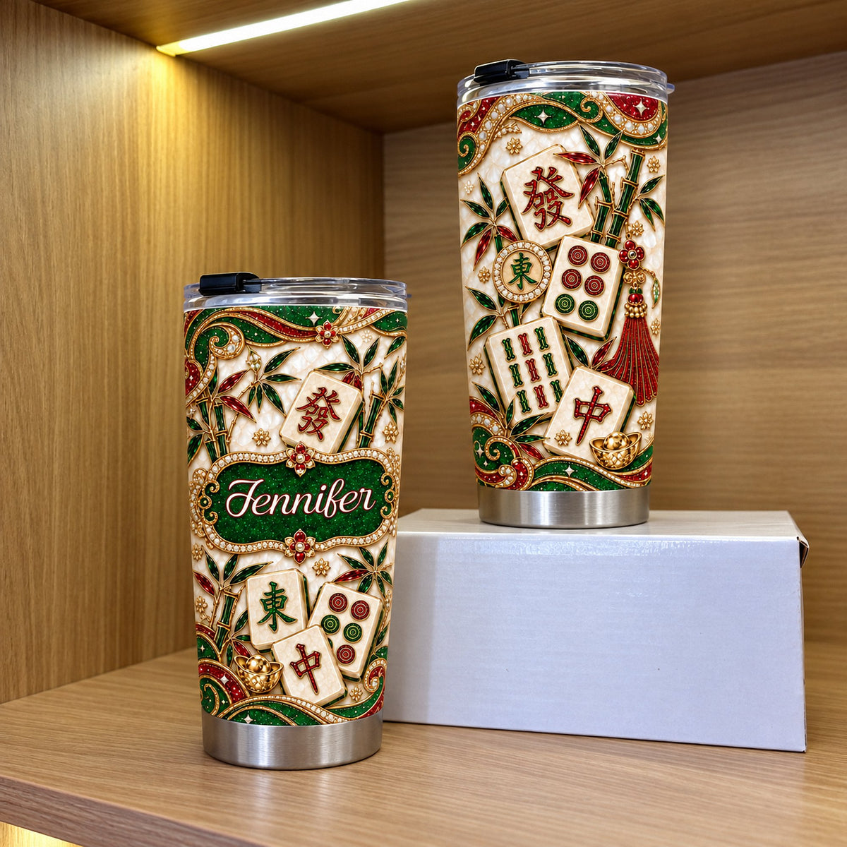 Two custom stainless steel tumblers with jeweled mahjong tile design standing on wooden shelf beside white box.