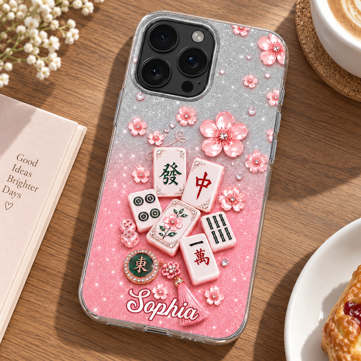 Glossy Mahjong Cherry Blossom phone case on wooden table next to notebook, coffee, and pastry.