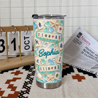 A coastal aesthetic tumbler stands on a woven mat next to a calendar and a newspaper.