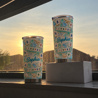 Two stainless steel tumblers stand on a windowsill during a warm sunset glow.