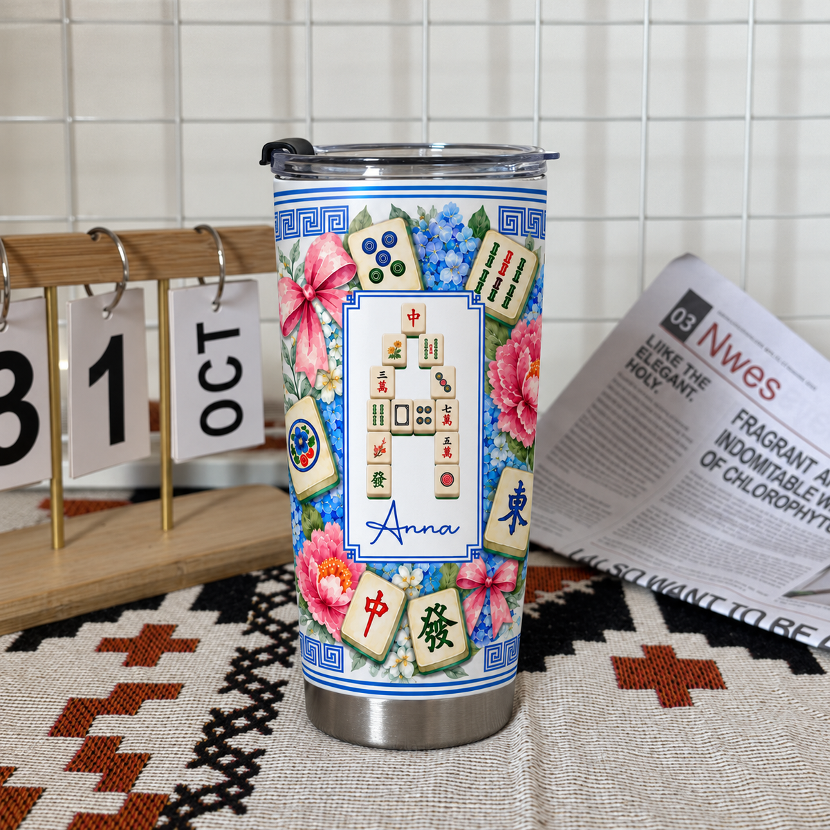 Mahjong Tile Number Floral Tumbler standing upright on a patterned cloth next to a calendar and open newspaper.