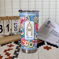 Mahjong Tile Number Floral Tumbler standing upright on a patterned cloth next to a calendar and open newspaper.