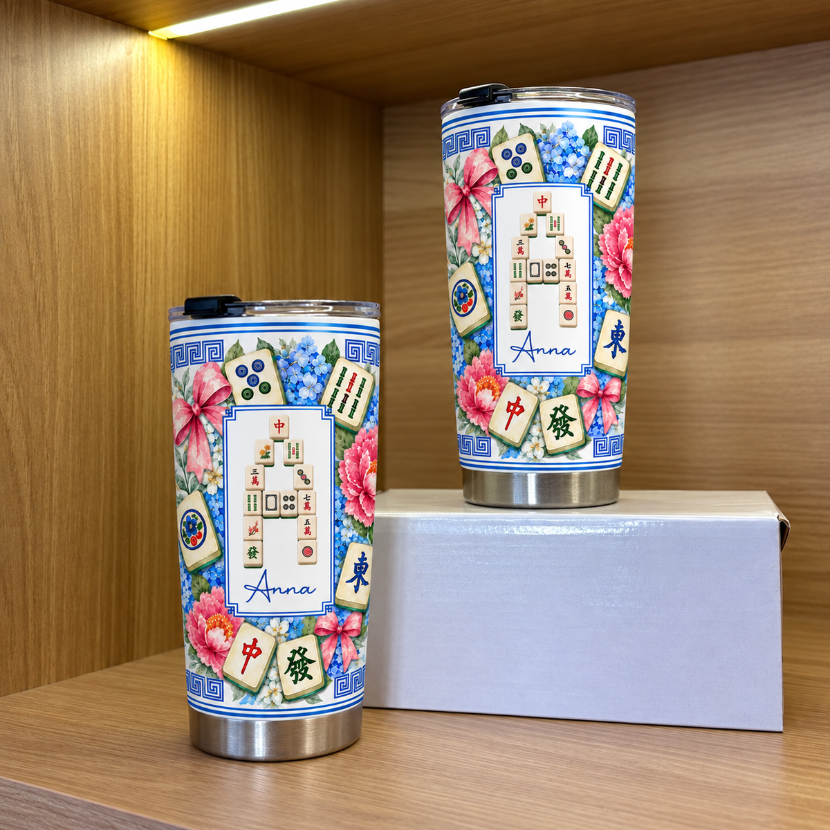 Two different sizes of the Mahjong Tile Number Floral Tumbler displayed on a wooden shelf next to a white box.